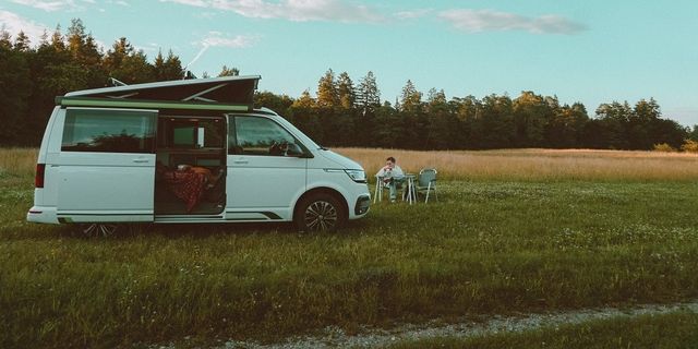 A man sits outside on a field next to a campervan