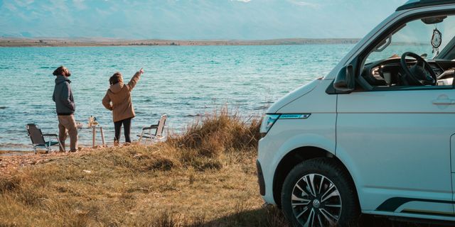 Zwei Personen mit Camper am See blicken in die Ferne