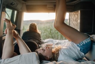 Kind liegt mit hochgestreckten Füßen im Camper beim Camping in Holland am Meer